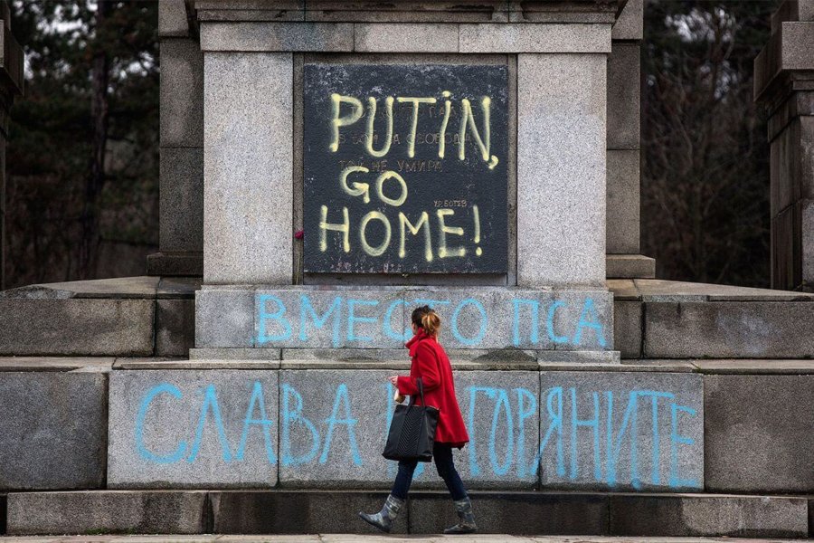 A woman walks past graffiti reading Putin go home on the Soviet Army Monument in Sofia, Bulgaria