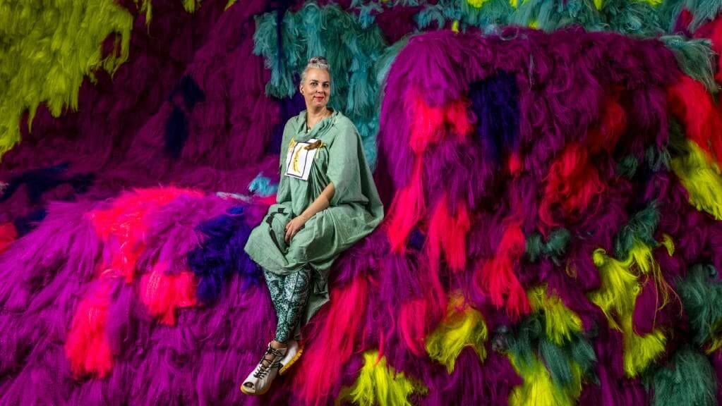 Artista Shoplfiter sentada en sus coloridas instalaciones Neverscape hecha con cabello
