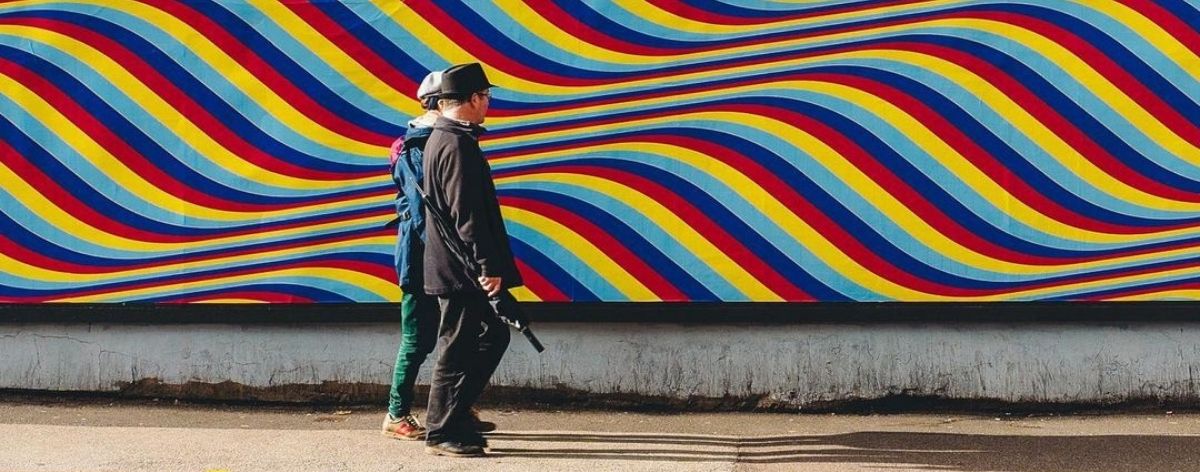 hombre y mujer con sombrero pasean frente a mural de colores