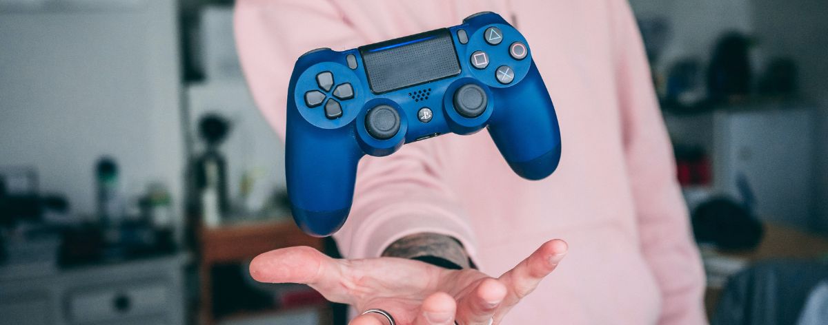 persona con hoodie rosa lanza con la mano un control de videojuegos color azul